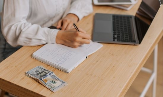 Persona che lavora con laptop, quaderno e soldi.
