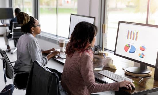 Persone analizzano dati su computer in ufficio moderno.