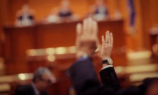 Votazione in aula parlamentare con mani alzate.