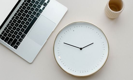 Orologio da parete, laptop e tazza su scrivania.