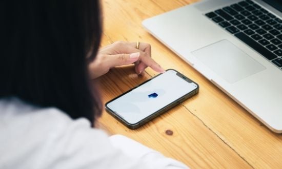 Donna usa smartphone e laptop su scrivania di legno.