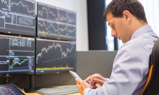 Uomo analizza grafici di borsa su computer e smartphone.