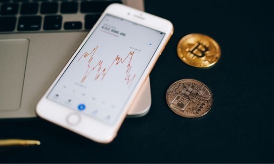Grafico criptovalute su smartphone con monete Bitcoin.