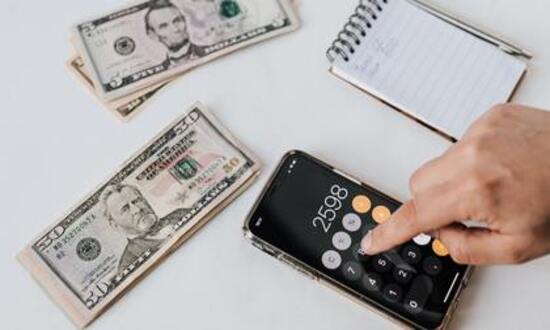 Calcolatrice su smartphone con banconote e taccuino.