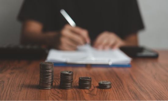 Monete impilate su tavolo con persona che scrive.