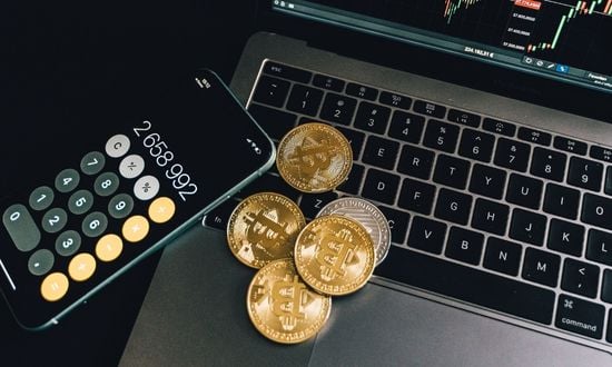 Criptovalute su laptop con calcolatrice e grafici finanziari.