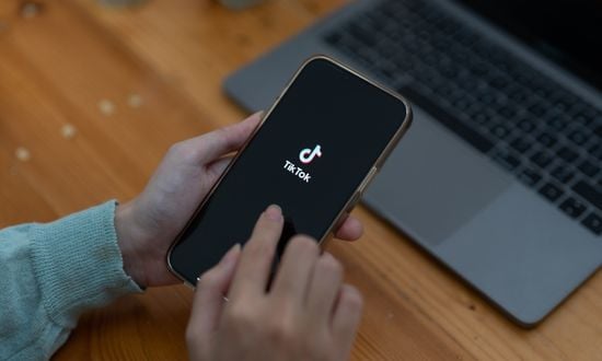 Persona usa TikTok su smartphone vicino a laptop.