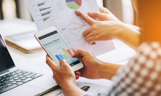 Analisi dati aziendali su smartphone e grafici cartacei.
