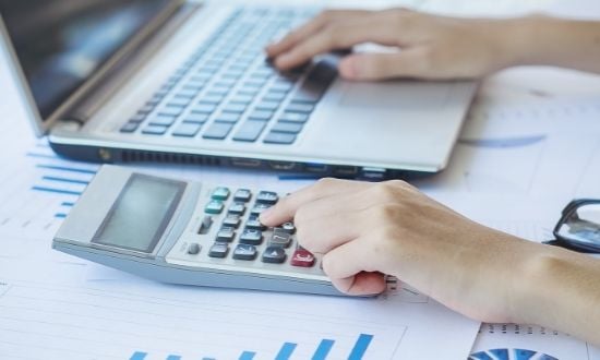 Persona che lavora con calcolatrice e computer portatile.