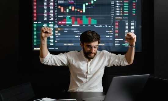 Uomo festeggia successo trading davanti a grafici finanziari.