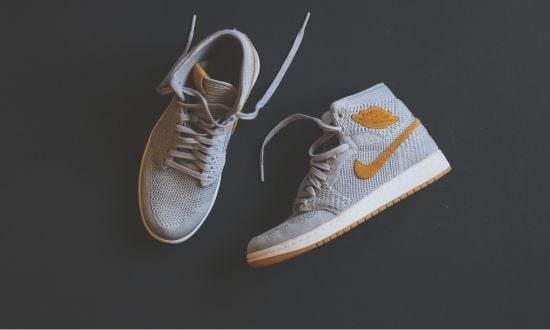 Scarpe sportive grigie con logo arancione su sfondo nero.