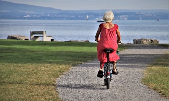 Anziana in bicicletta lungo un sentiero vicino al lago.