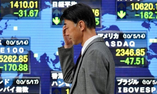 Uomo preoccupato davanti a schermi di borsa in calo.