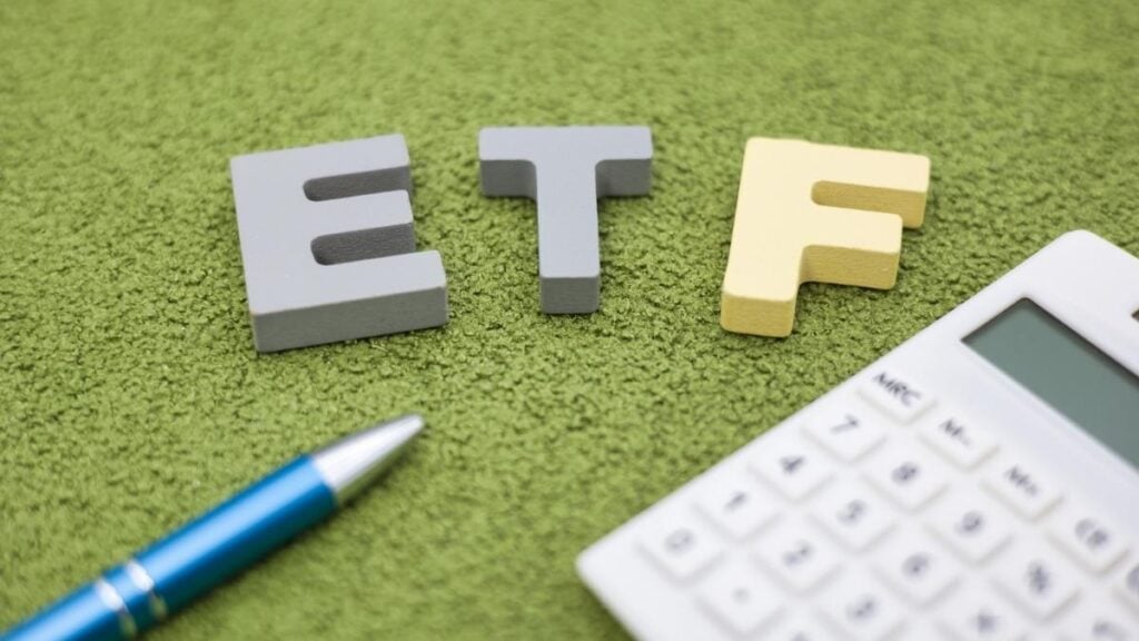 scritta etf su fondo verde con penna e calcolatrice